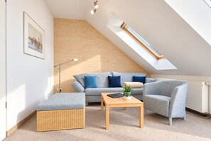 Quarto moderno estilo loft com teto inclinado, sofá seccional cinza, mesa de centro de madeira e um banquinho de vime.