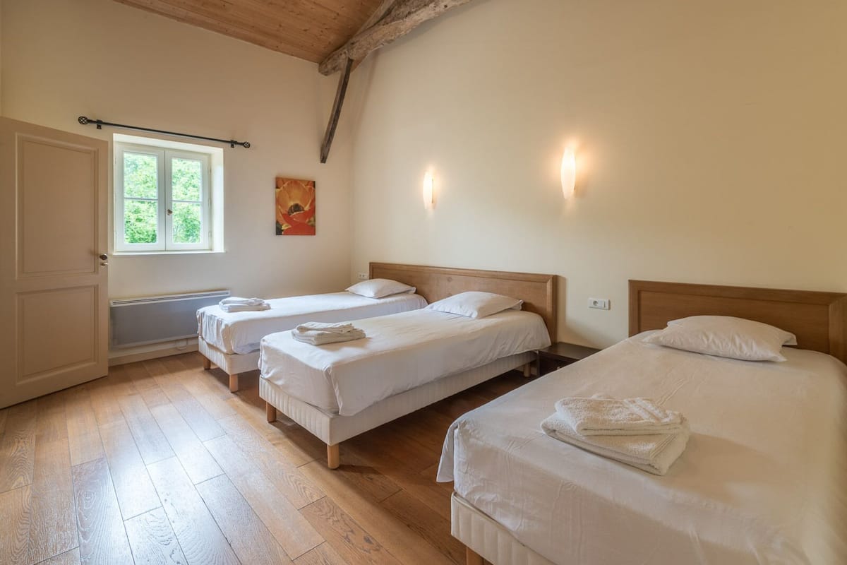 Une chambre avec trois lits, une fenêtre donnant sur un espace verdoyant et un radiateur.