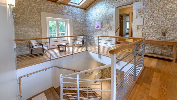 Un loft espacioso con piso de madera, paredes de piedra, tragaluces y un balcón con barandilla.