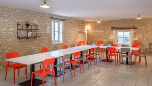 Un salón de conferencias con una larga mesa y numerosas sillas, paredes de piedra y una ventana.