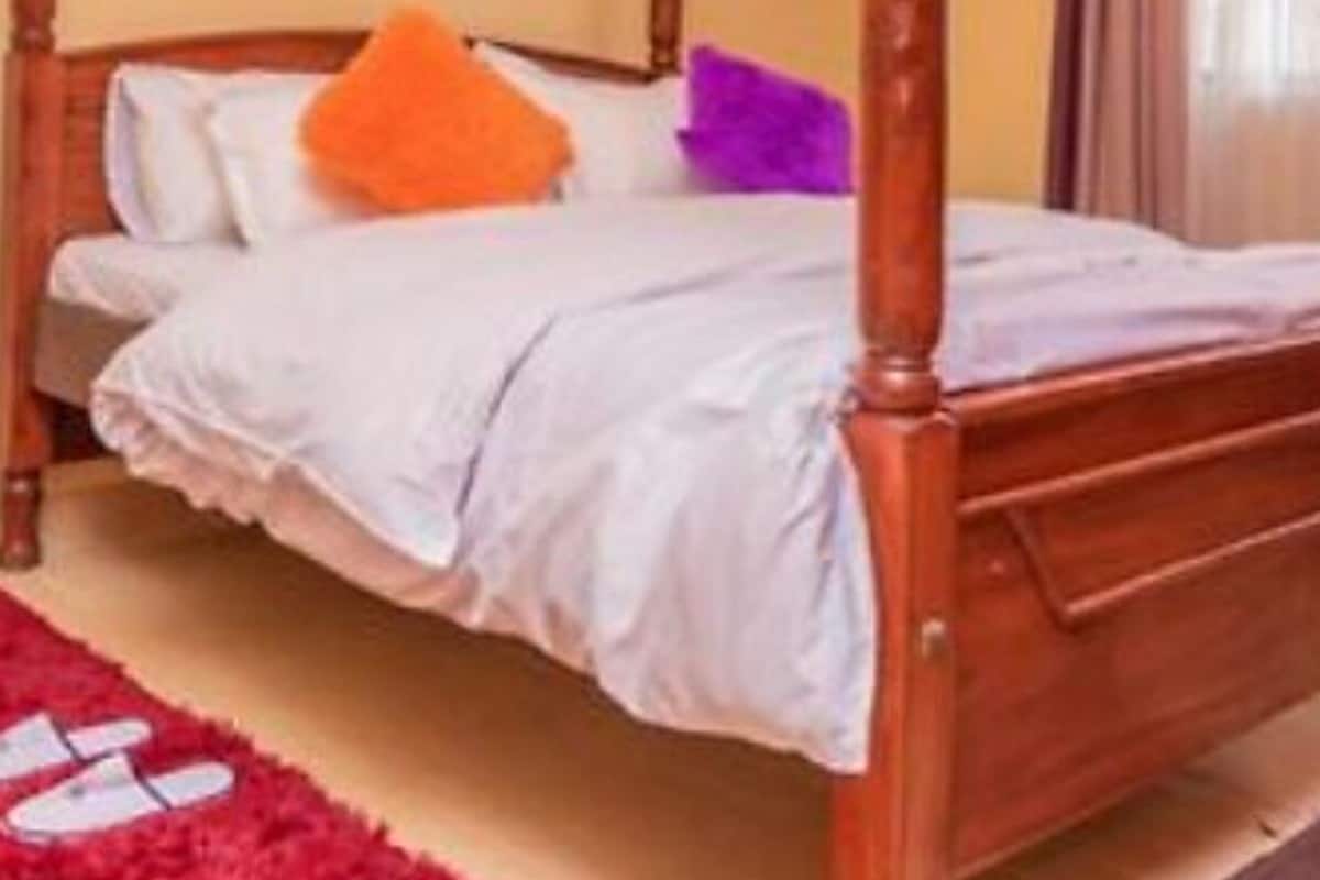 A wooden four-poster bed in a room with yellow walls, a red rug, and a window with curtains.