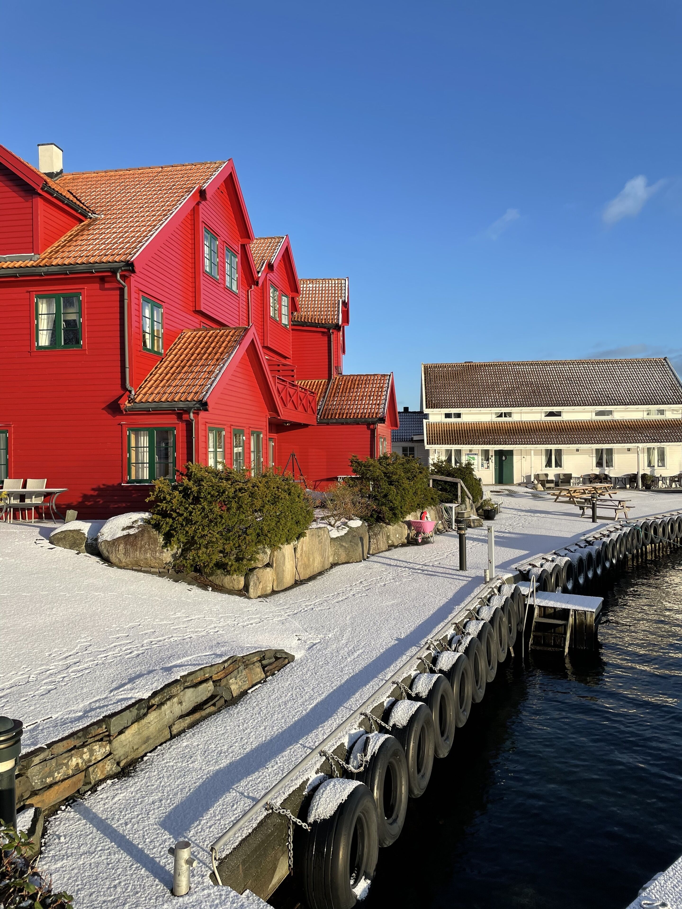 A red building with a tiled roof, a dock with tires, and a clear blue sky.
