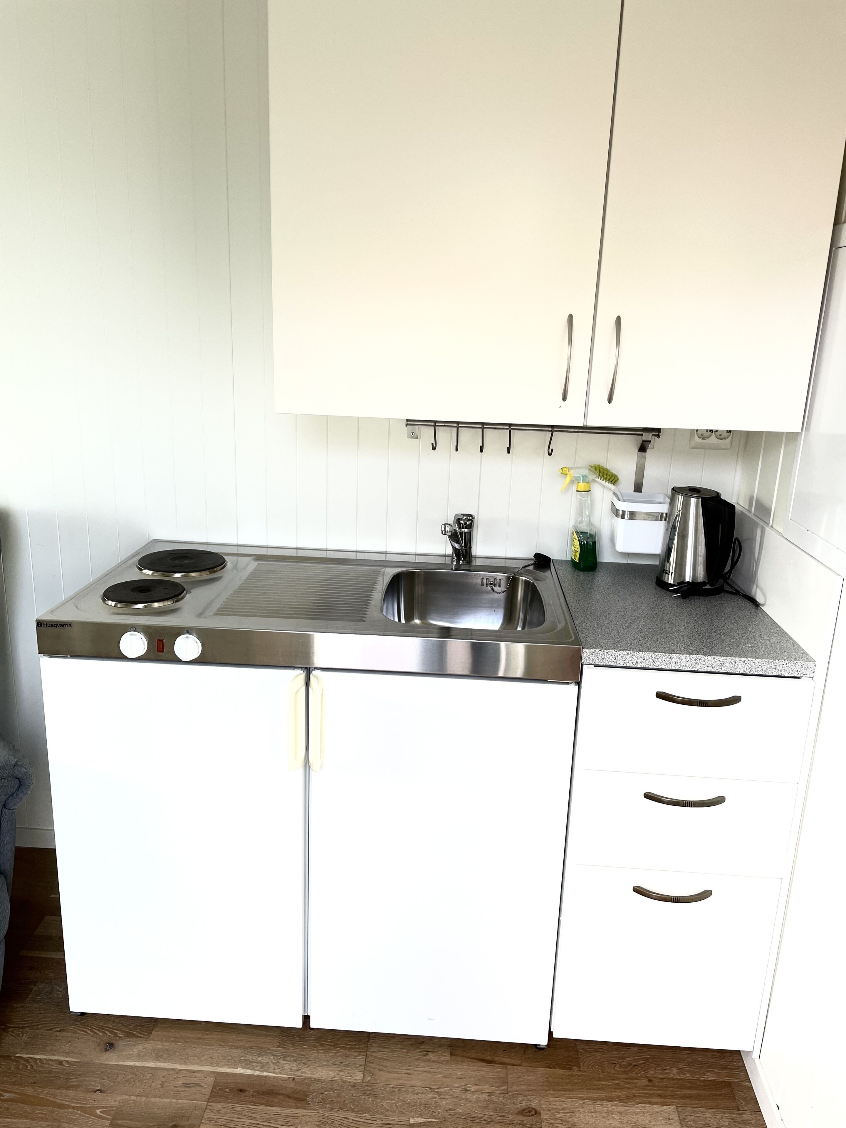 Una cocina compacta con estufa de acero inoxidable, un lavamanos y muebles de color blanco.