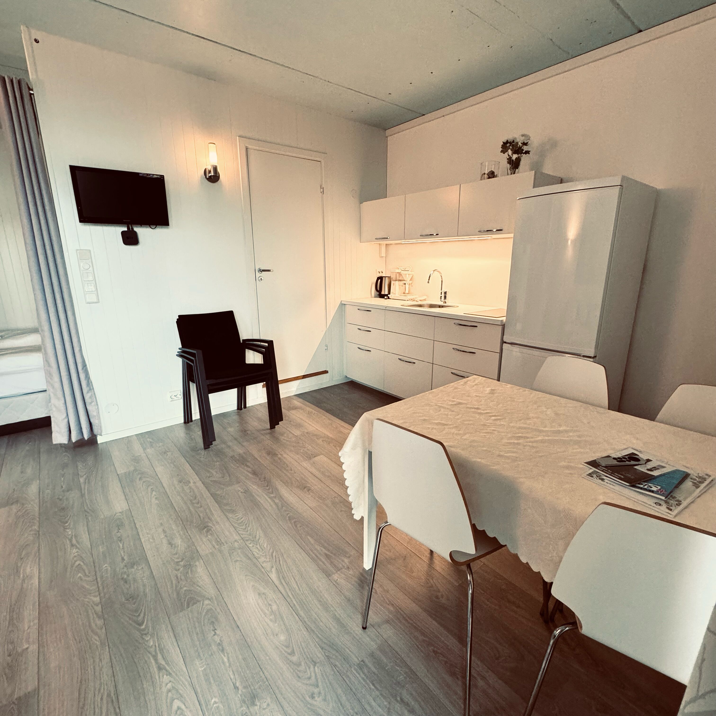 A compact, modern room with a kitchenette, a dining area, and a single bed.