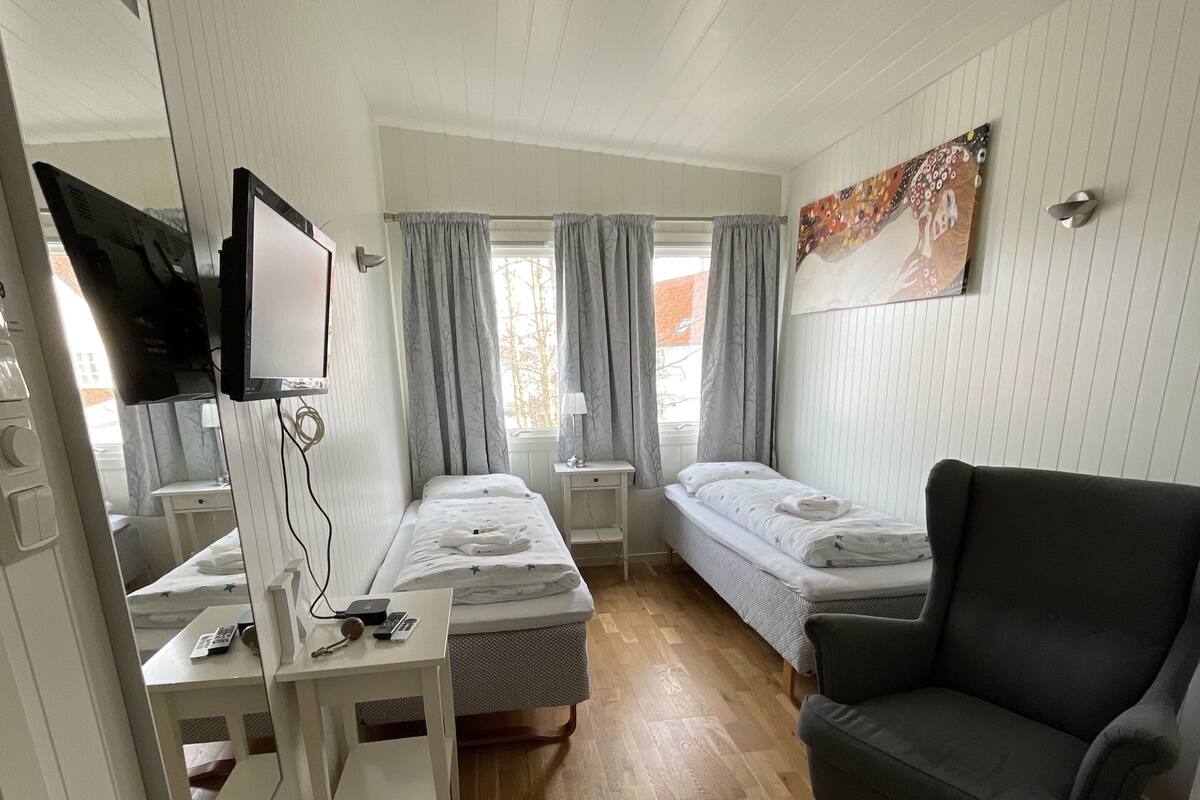 A room with two beds, a desk with a computer, a chair, and a TV mounted on the wall.