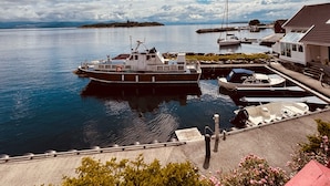 A harbor with boats docked, a small island in the distance, and a building with a red roof.
