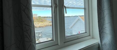 Una habitación con ventana que da a una masa de agua y una costa lejana.