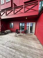 A red building with a wooden deck, a glass door, and a table with chairs.