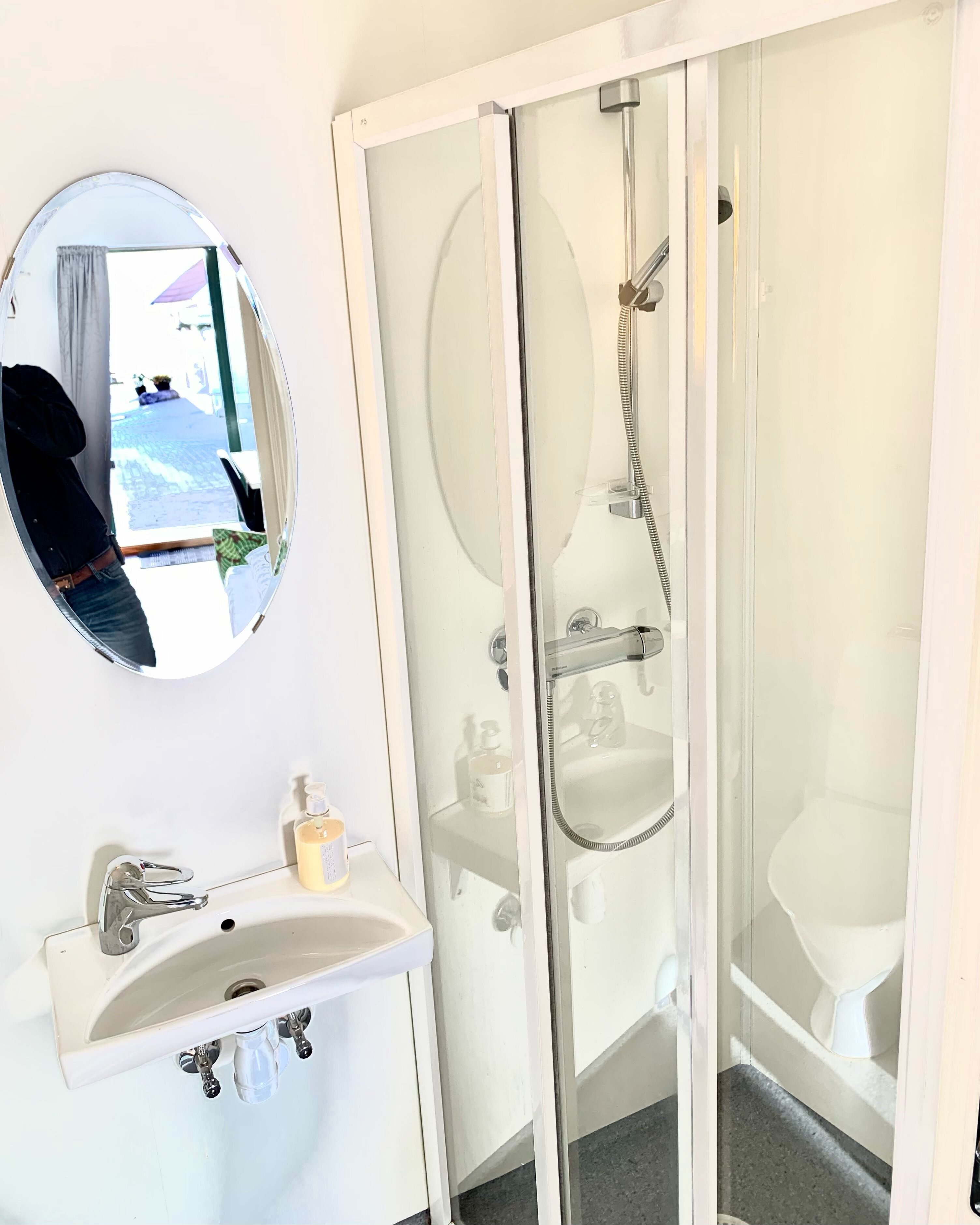 A bathroom with a white sink, a round mirror, and a glass-enclosed shower area.