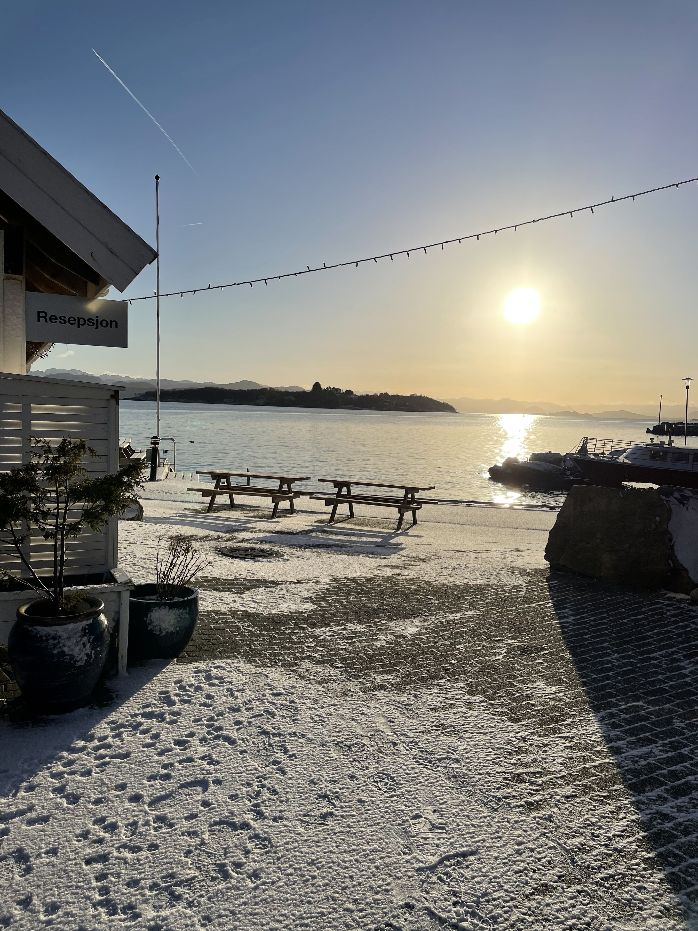 A waterfront view with a bench area, a sign reading "Resepjon," and a clear sky.