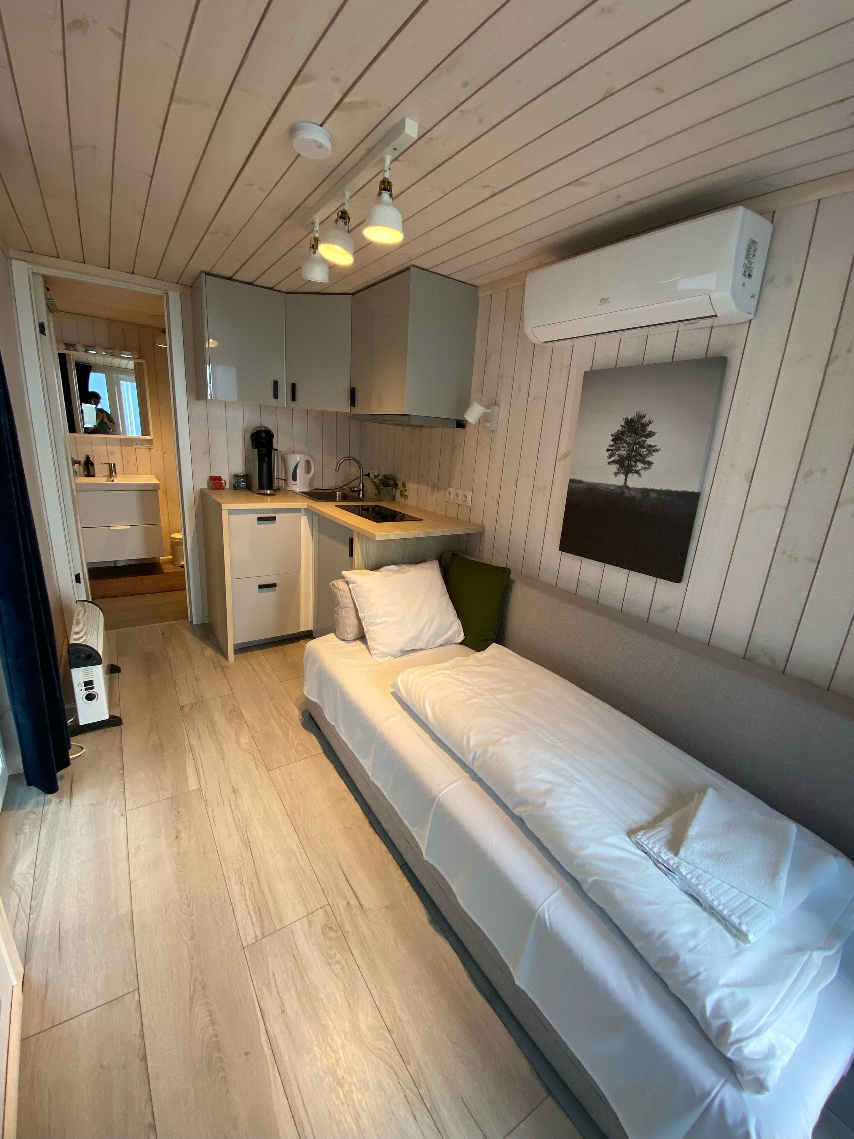 A compact room with a bed, a small kitchenette, and a mirror.