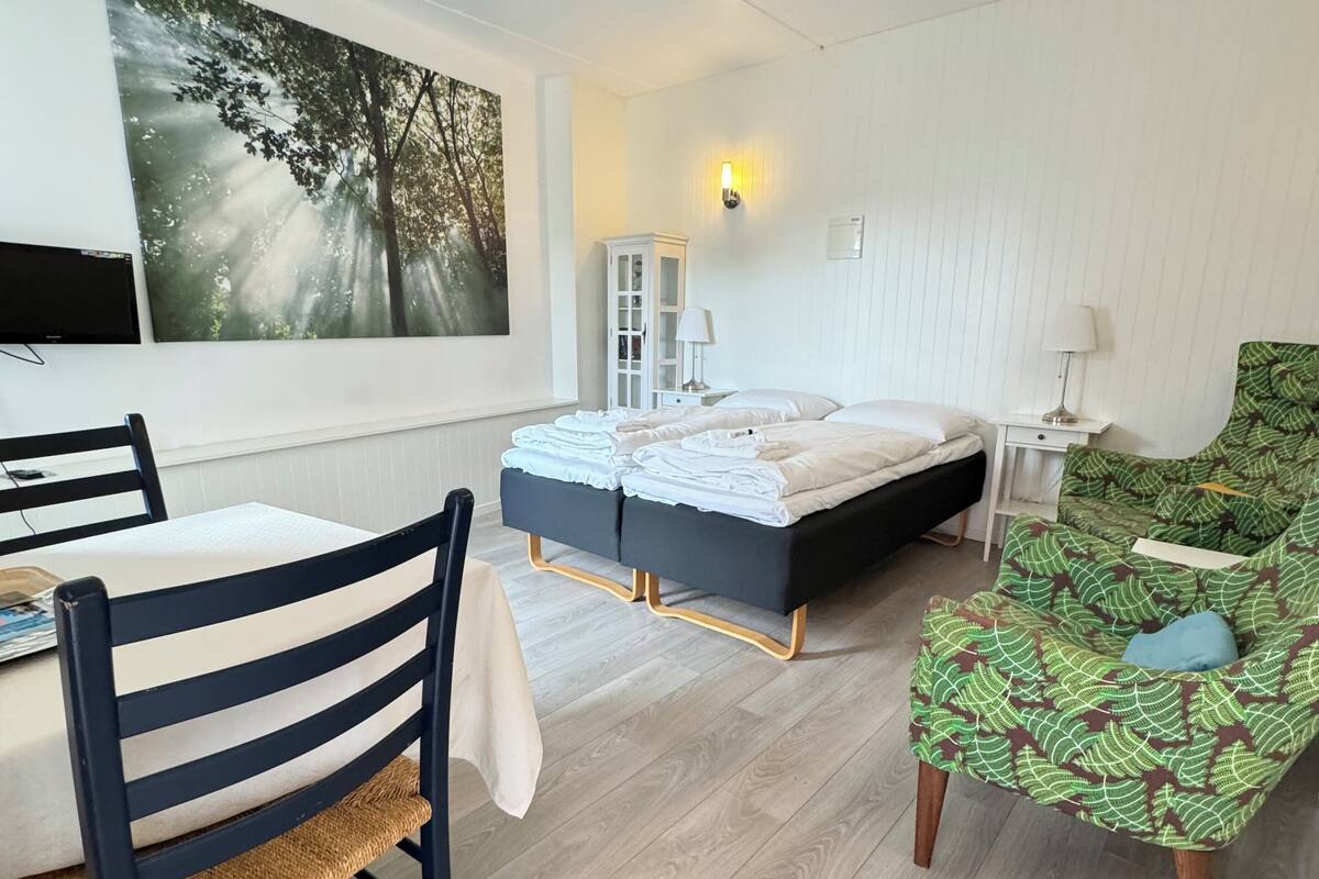 A room with a bed, a chair, a table, and a wall-mounted TV.