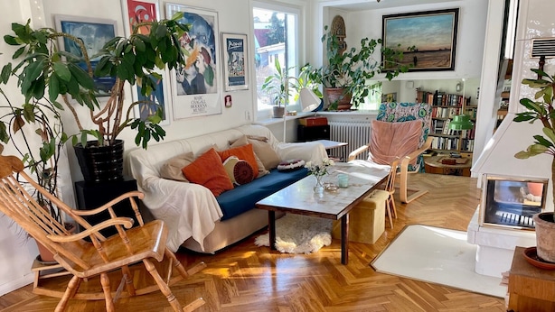 Un salon chaleureux avec un parquet en bois disposé en chevrons, un canapé blanc agrémenté de coussins colorés, un fauteuil à bascule et une table basse.