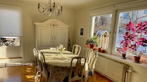 Une salle à manger avec une table ronde, des chaises blanches, un lustre et des plantes en pot près de la fenêtre.