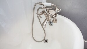 Eine weiße Badewanne mit einem Wasserhahn und Duschkopf im Vintage-Stil, einem Abfluss und einem flexiblen Schlauch.