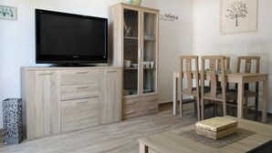 Een woonkamer met een flatscreen televisie, houten kasten, een eettafel met stoelen en een aan de muur hangend kunstwerk.