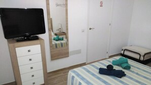 Een slaapkamer met een bed, een televisie op een houten kast, een spiegel en een kledingkast.