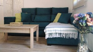 Een woonkamer met een blauwgroene bank, een houten salontafel, een gestreept plaid en een vaas met bloemen.