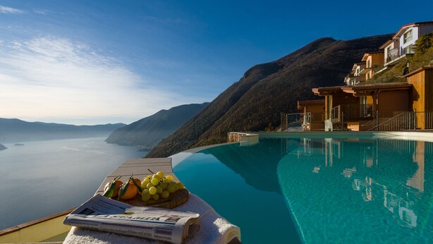 A poolside with a newspaper and fruit, overlooking a body of water and mountains. - EnjoyIseoLake - Colosseum - Parzanica (Parzanica)