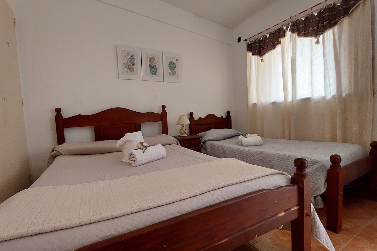 A hotel room with two wooden beds, a nightstand, a lamp, and a window with curtains.