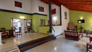 Un vestíbulo amplio con techo alto, paredes verdes, muebles de madera y una escalera que conduce a otra zona.