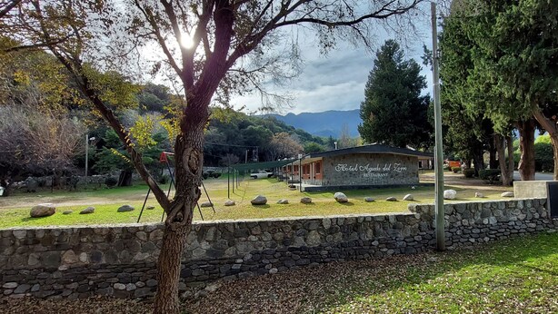 Un muro de piedra, una zona con césped y un edificio con la inscripción "Hotel Agua del Loro Restaurant".