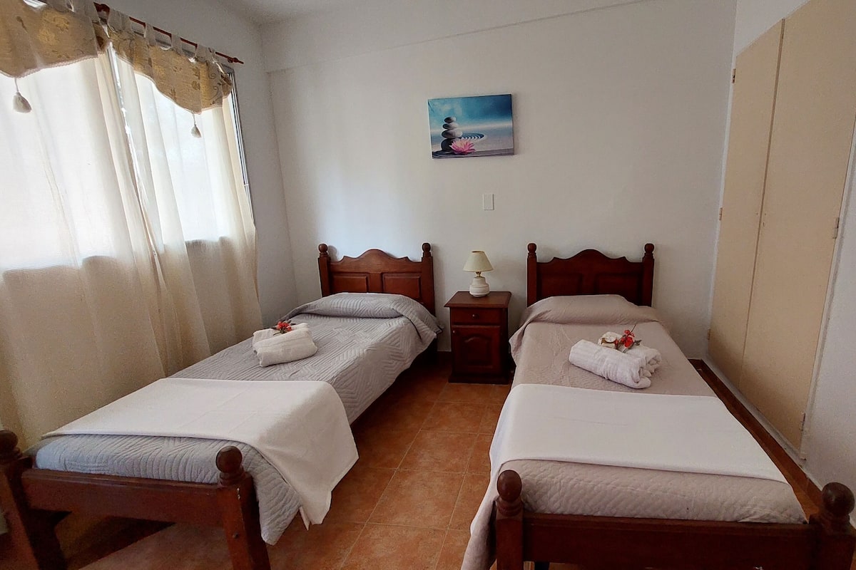 A room with two wooden beds, a nightstand with a lamp, and a painting on the wall.