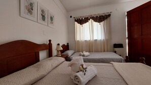 Habitación con dos camas, cabecera de madera, mesita de noche con lámpara y ventana con cortinas.