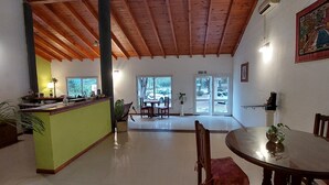 Amplia habitación con techo de madera, pared de acento verde, zona de comedor con mesa y sillas redondas, y vista al exterior a través de una puerta de vidrio.