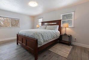 Een slaapkamer met een houten bed, twee bedlampen, een vloerkleed en een raam met uitzicht op bomen.