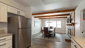 Eine moderne Küche mit Edelstahlkühlschrank, Holzbalken an der Decke, einem Essbereich mit Tisch und Stühlen sowie einem Kamin.