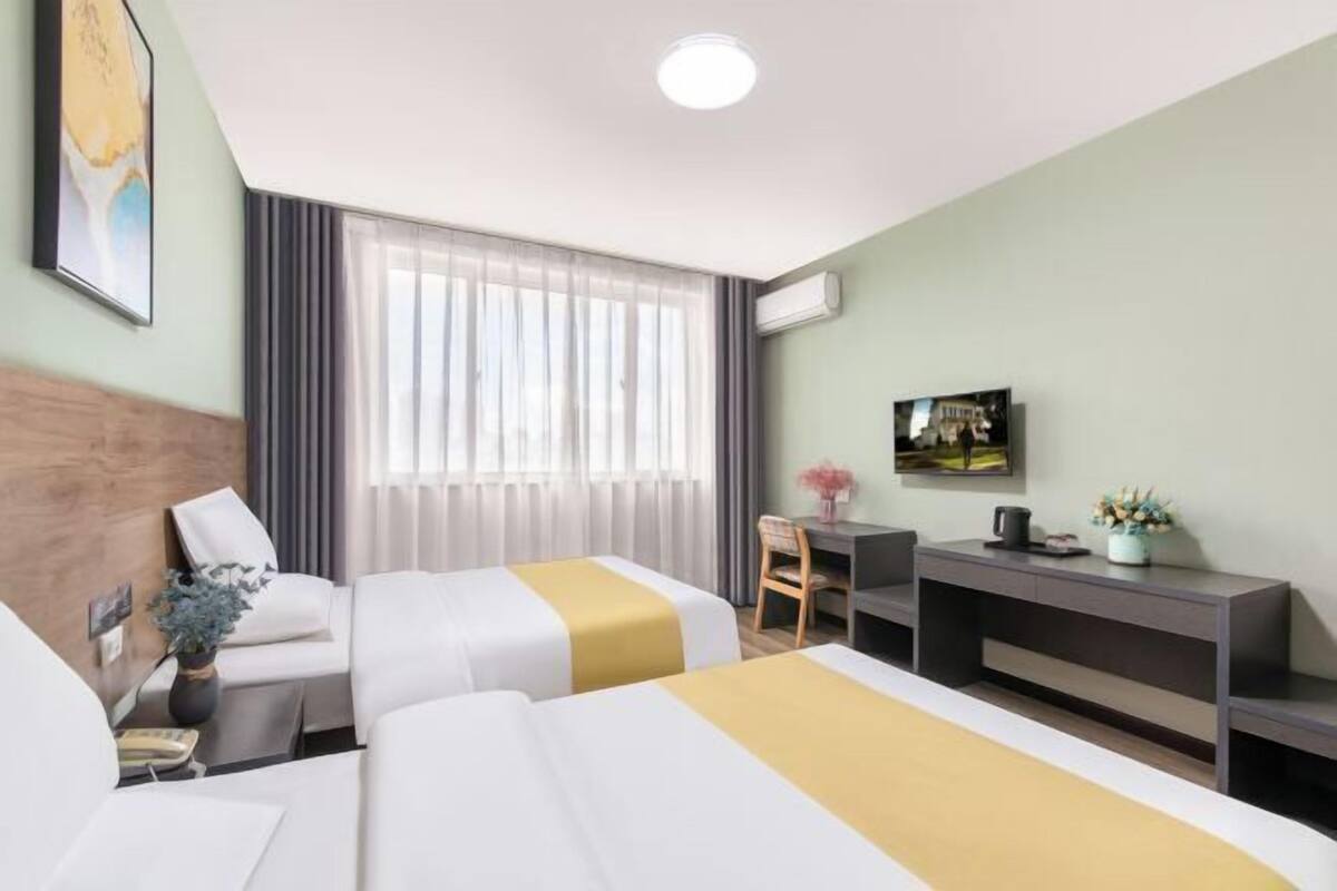 A hotel room with two beds, a desk, a chair, a TV, and a window with curtains.