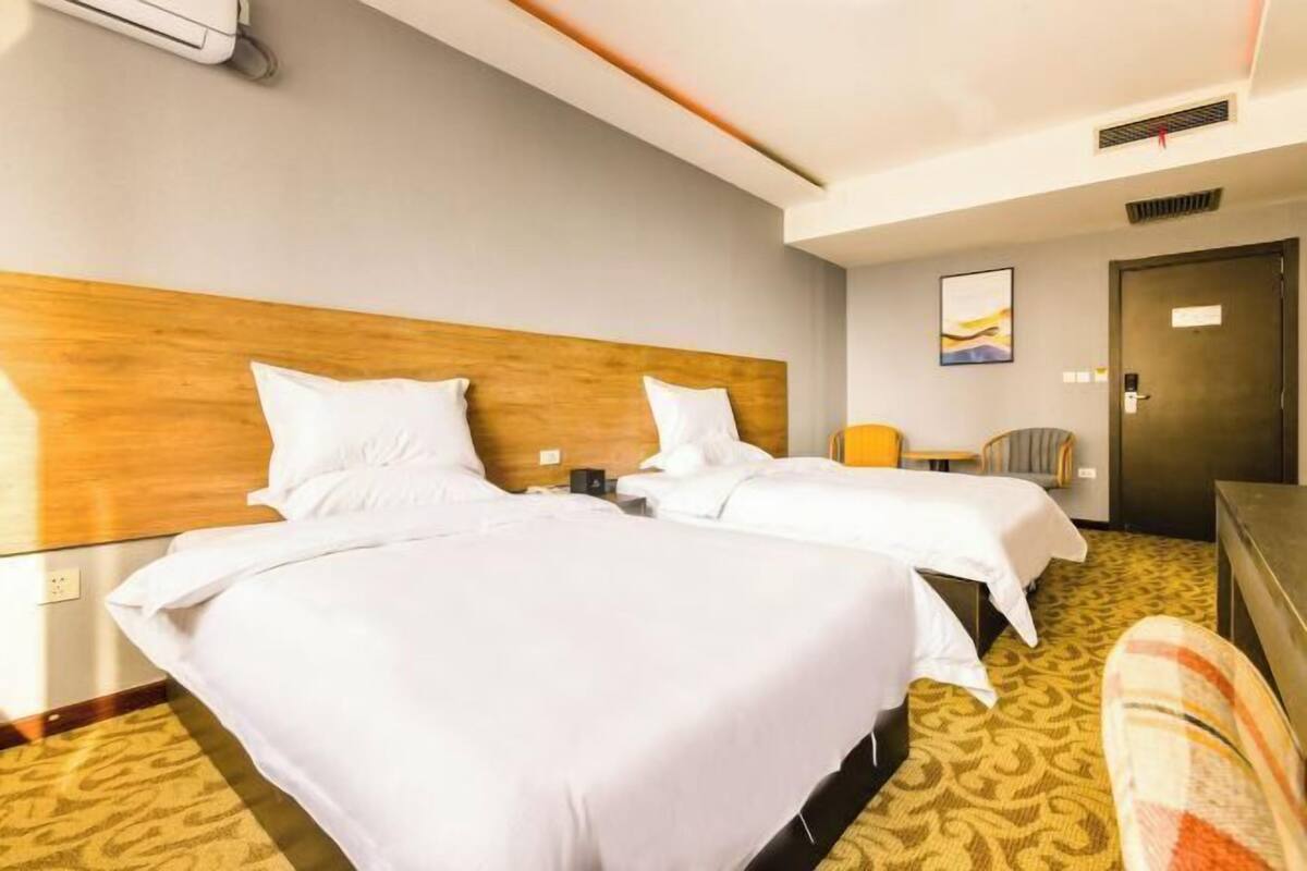 A hotel room with two beds, a wooden headboard, a small table, a chair, and a door.