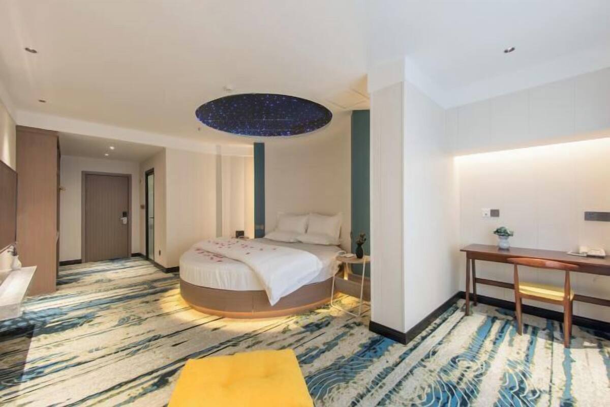 A modern hotel room with a round bed, a desk, and a unique ceiling light fixture.