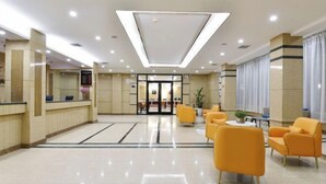 Egy szállodai előtér, amelyben található egy recepciós pult, egy ülősarok és egy nagy, üvegportálos bejárat.