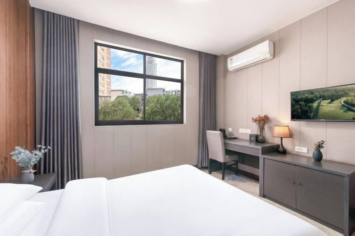 A hotel room with a bed, a desk, a chair, a TV, and a window with a city view.