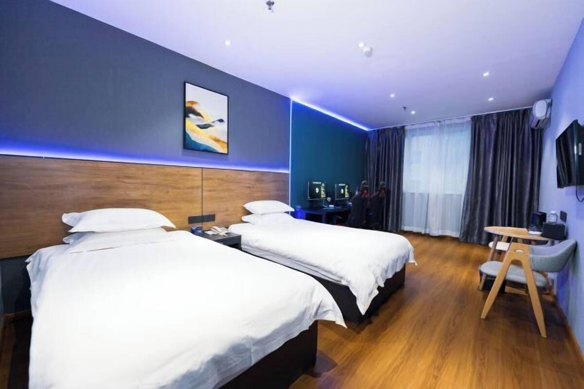 A hotel room with two beds, a desk, a chair, a TV, and a window with curtains.