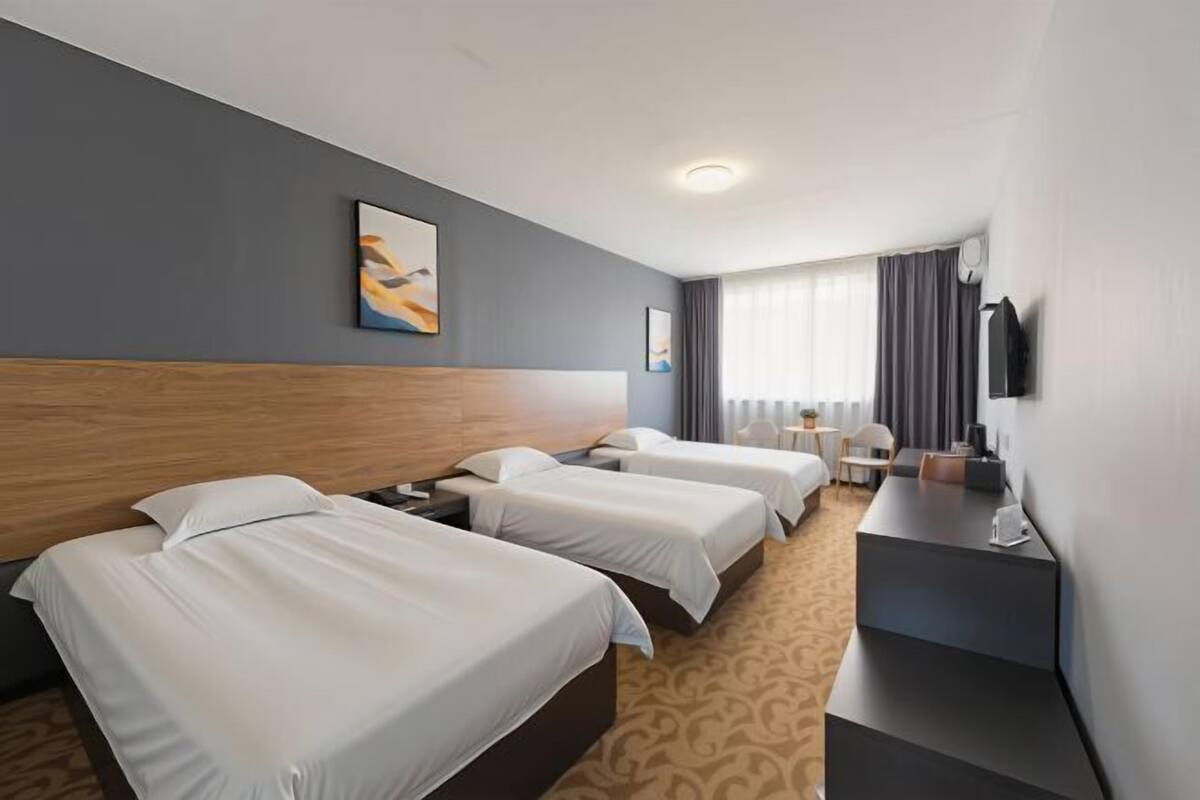 A hotel room with three beds, a desk, a TV, and a window with curtains.