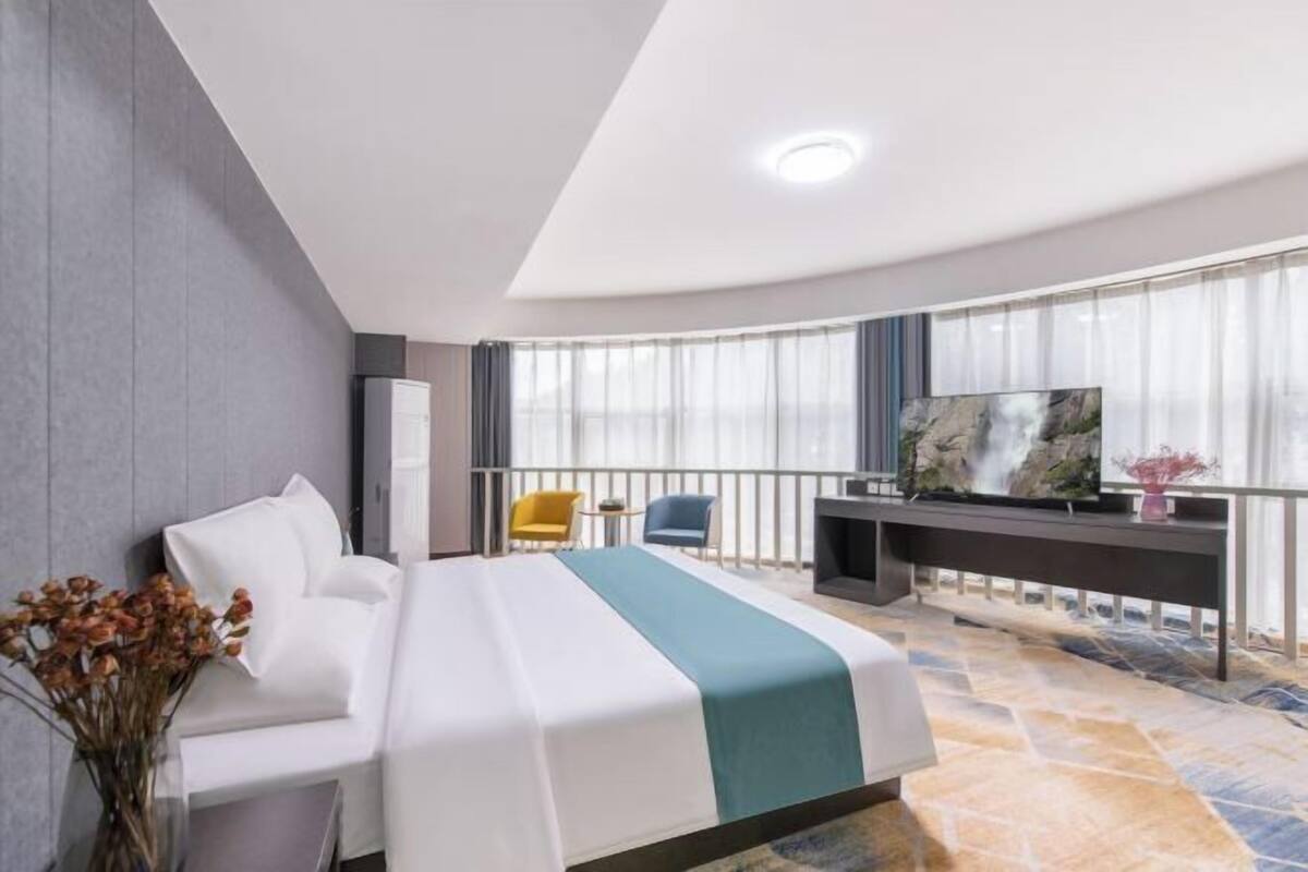 A hotel room with a bed, a desk, a TV, and a balcony with chairs.