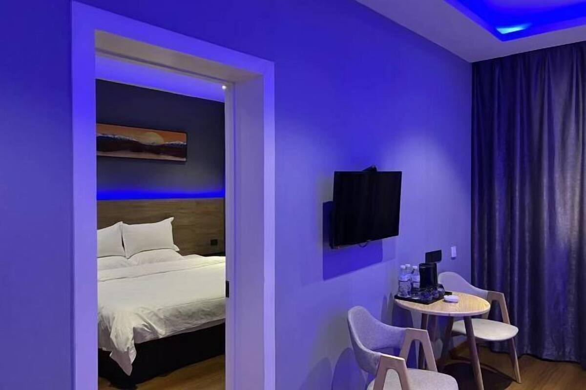 A hotel room with a bed, a TV mounted on the wall, a small round table with chairs, and a painting above the bed.