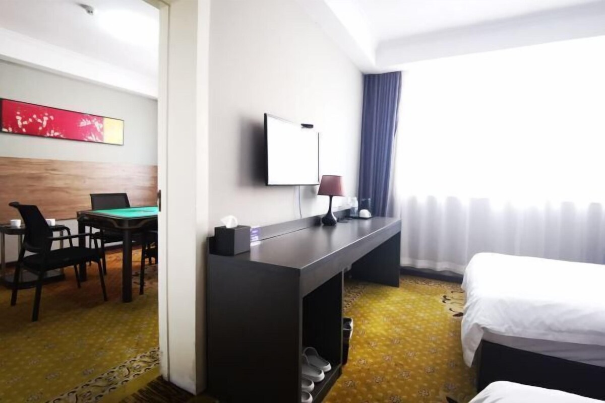 Camera d'albergo con un letto, una scrivania con un computer, una sedia, una TV e una finestra con tende.