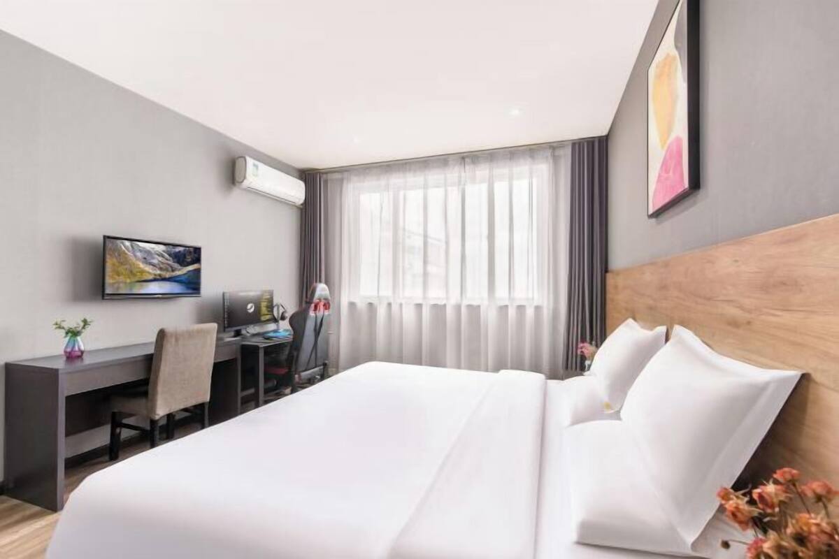A hotel room with a bed, desk, chair, and a television on the wall.