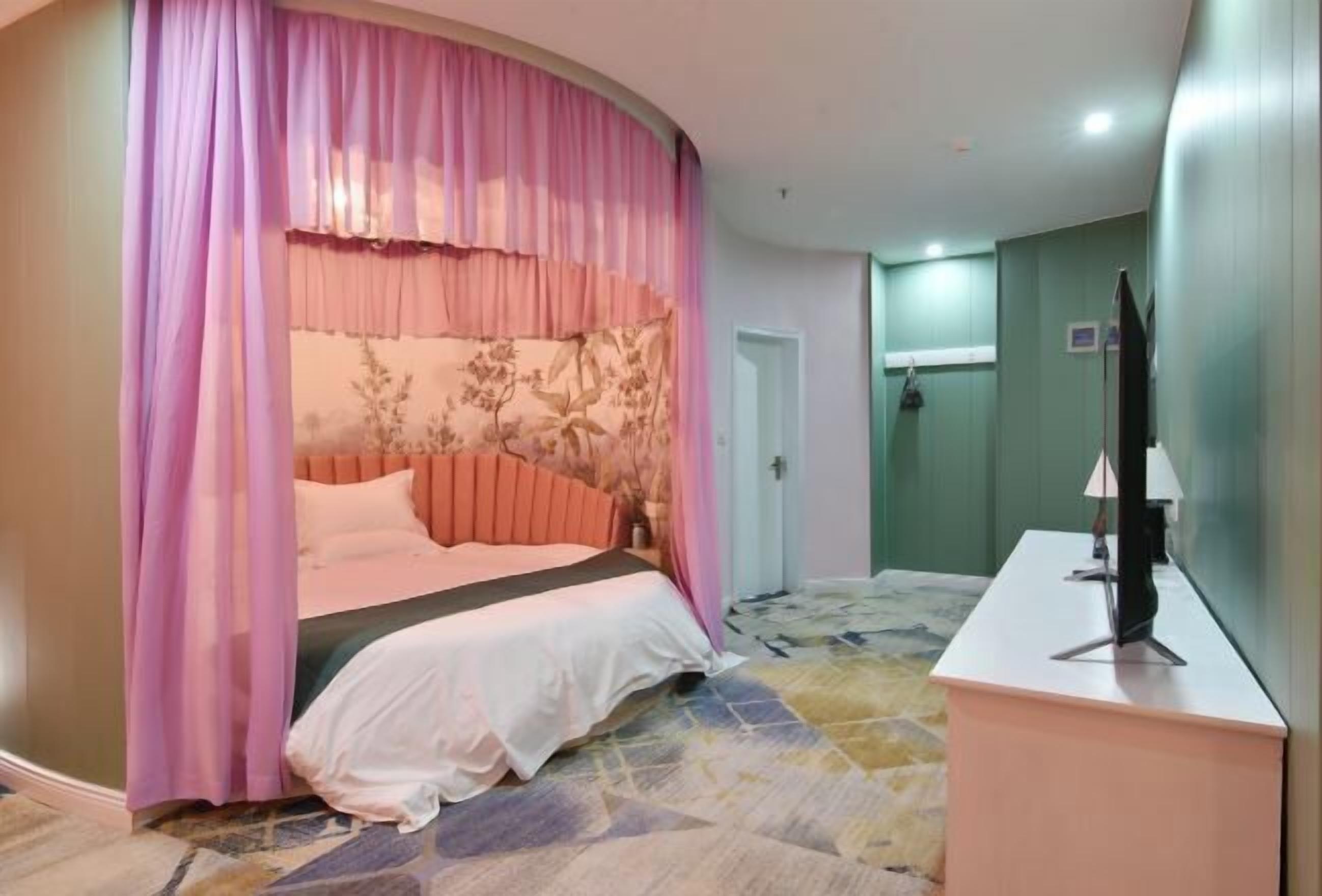 A bedroom with a bed, curtains, a bedside table, a TV, and a shower area.