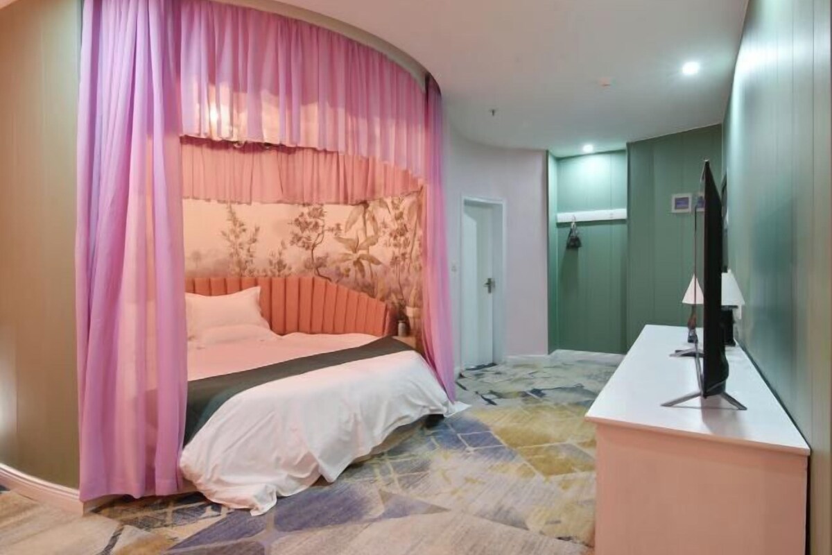 Una camera da letto con un letto, tende, un comodino, una TV e un angolo doccia.