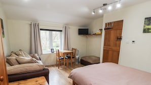 A cozy room with a bed, a sofa, a wooden table, a small table, a chair, a television, and a window with curtains.