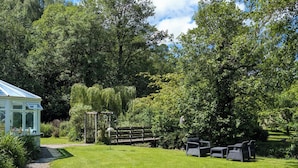 A conservatory with a glass roof, surrounded by lush greenery and a wooden fence.