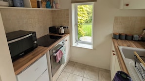 A compact kitchen with a microwave, toaster, and kettle, a window with a view of greenery, and a small dining area with a table and chairs.
