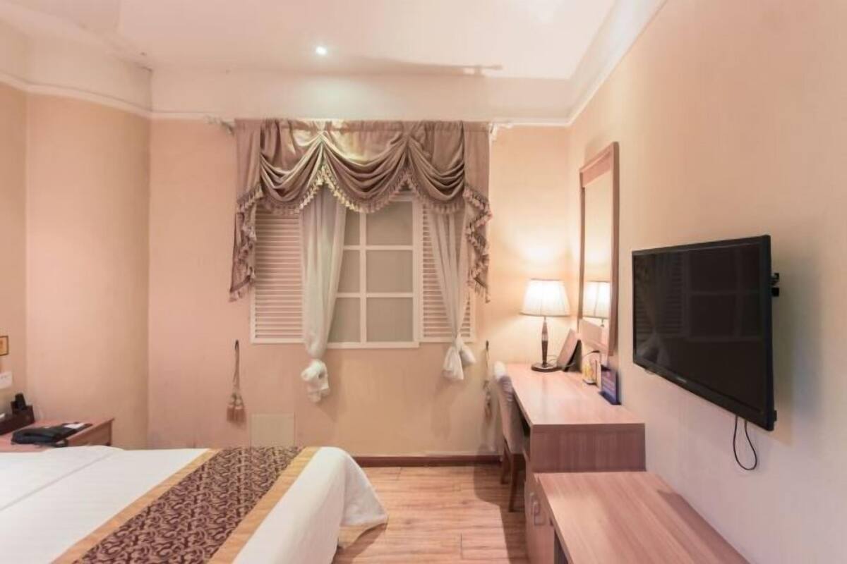 A hotel room with a bed, desk, TV, and window with curtains.