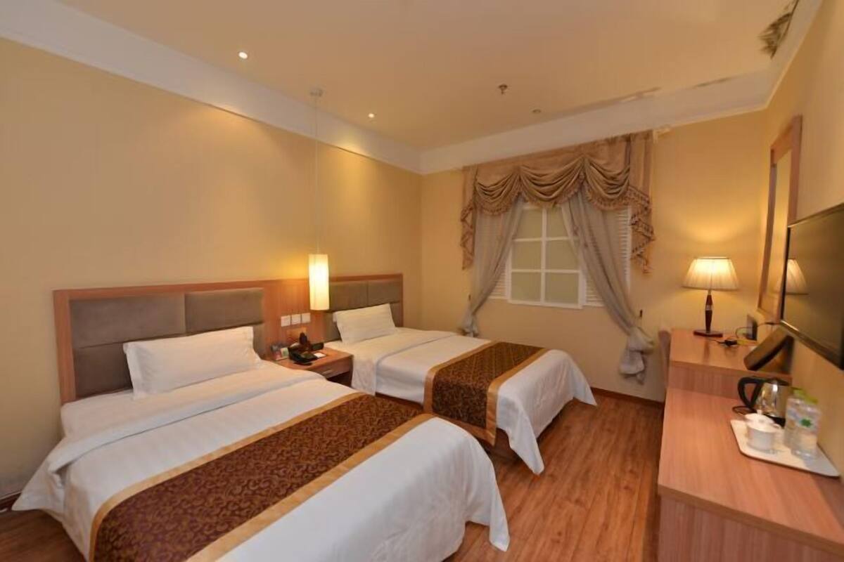 A hotel room with two beds, a wooden desk, a mirror, and a window with curtains.