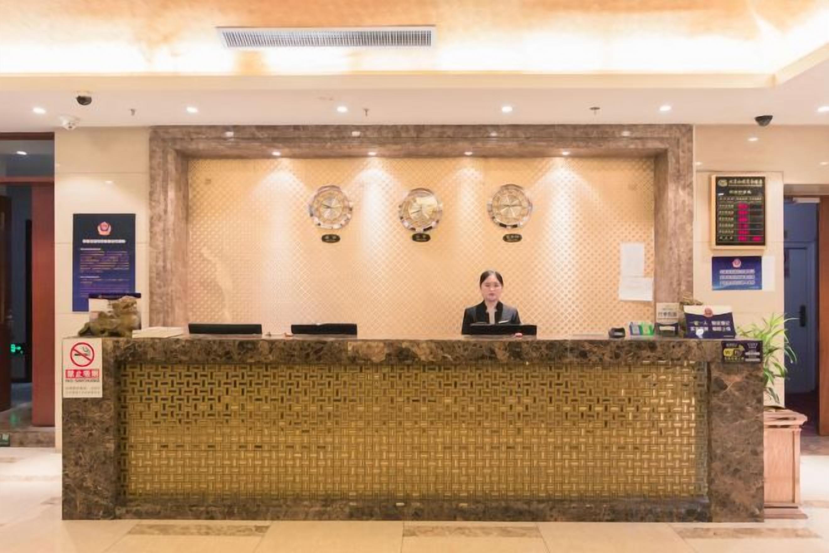 A reception desk with a receptionist, a wall-mounted clock, and a sign with room information.